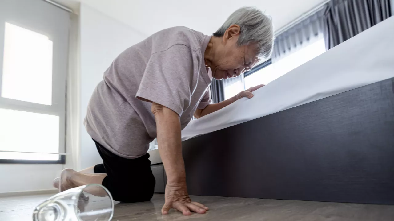 Elderly woman struggling to get up from the floor after falling due to vertigo or balance disorder — illustrating the serious fall risk of dizziness in older adults