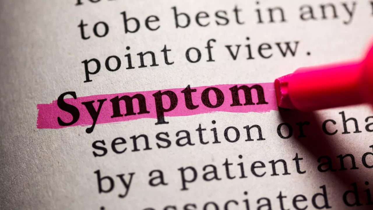 Medical dictionary with the word 'Symptom' highlighted in pink — representing clinical symptom assessment in vertigo diagnosis