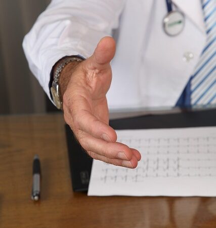 Doctor in white coat offering a handshake across a desk — Vertigo Doctor in Varanasi | Dr. Prateek Porwal, ENT